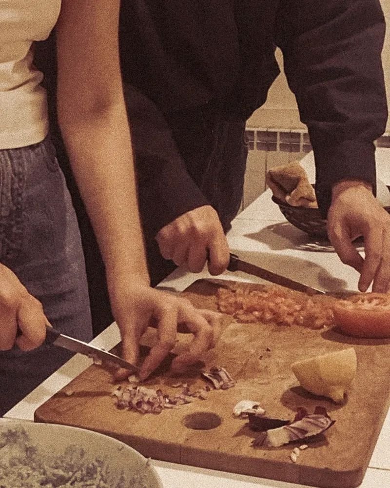 Una pareja picando cebolla y tomate sobre una tabla de madera